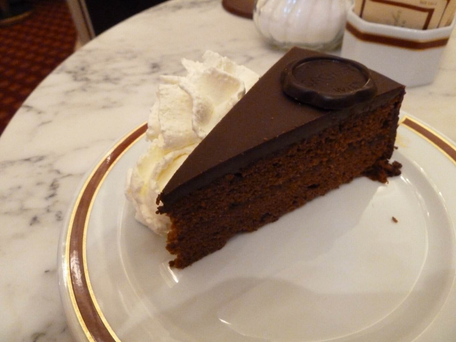 Stück Original Sacher-Torte mit Schlagobers auf einem Marmortisch im Café Sacher