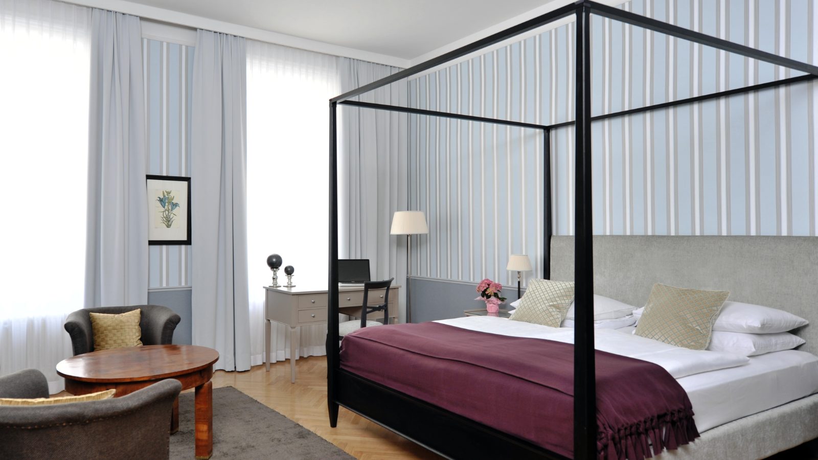 Christiane Hörbiger Suite im Hotel Kärntnerhof mit schwarzem Himmelbett, Schreibtisch und zwei Fauteuils vor hellblauer Streifentapete