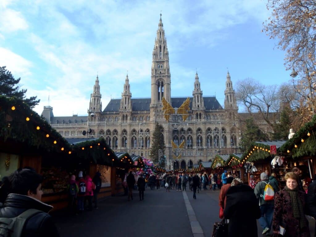 Vienna City Hall with a Christmas market in the foreground and twinkling lights along stalls.