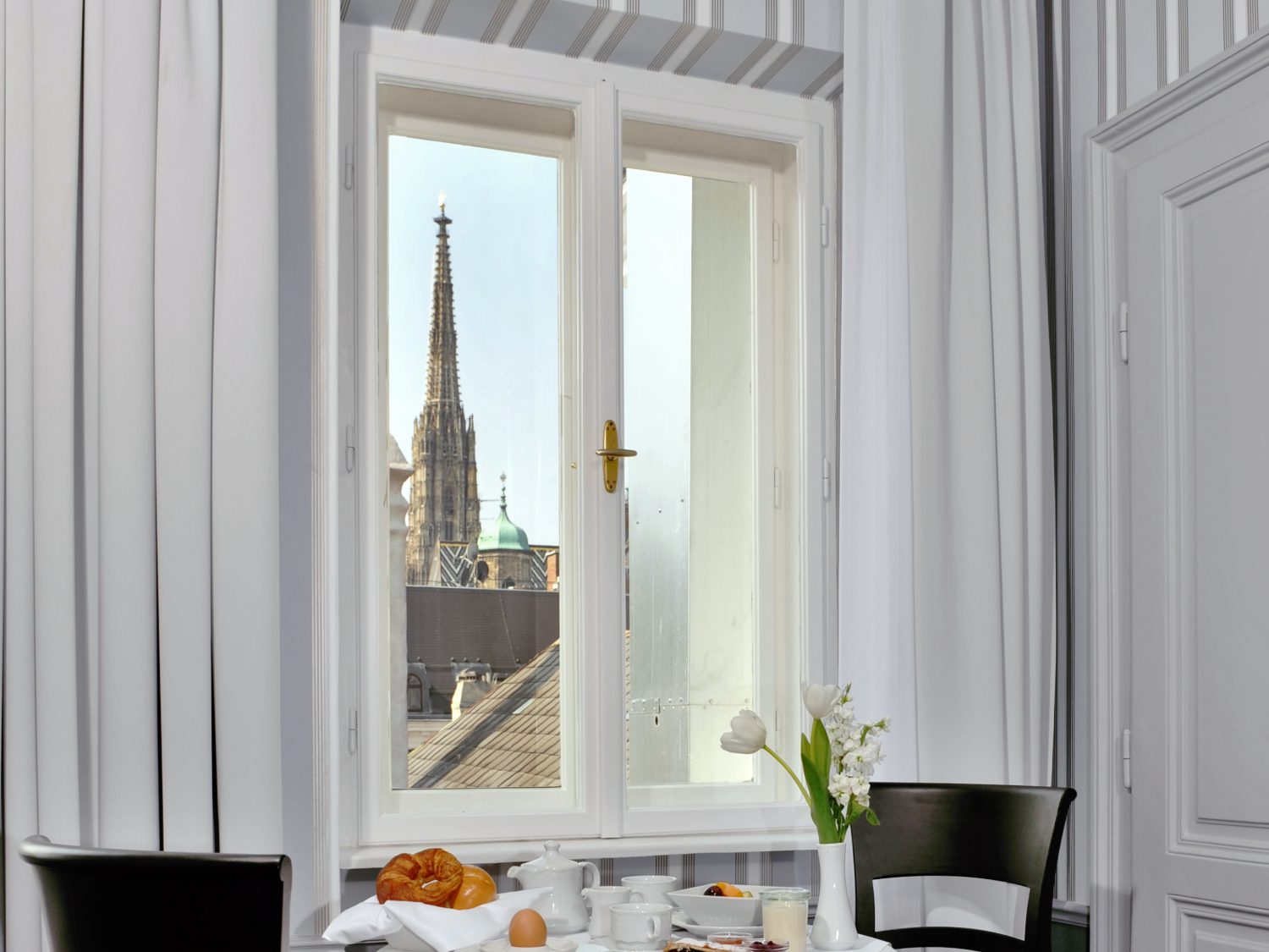 Gedeckter Frühstückstisch am Fenster der Dom Suite, dahinter der Südturm des Stephansdoms über den Dächern der Wiener Innenstadt