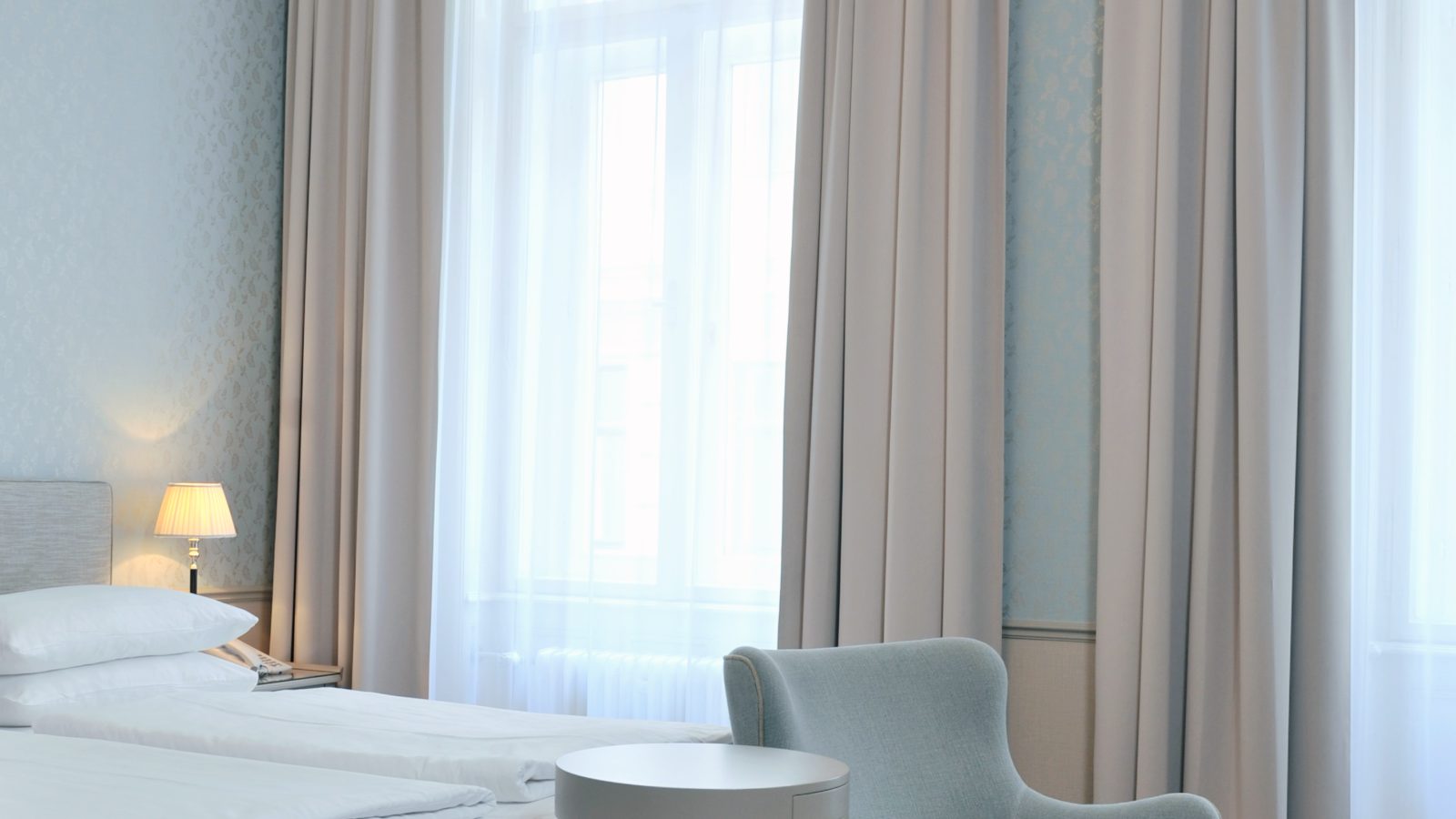 Helles Doppelzimmer im Hotel Kärntnerhof mit hohem Altbaufenster, Fischgrätparkett und hellblauem Fauteuil