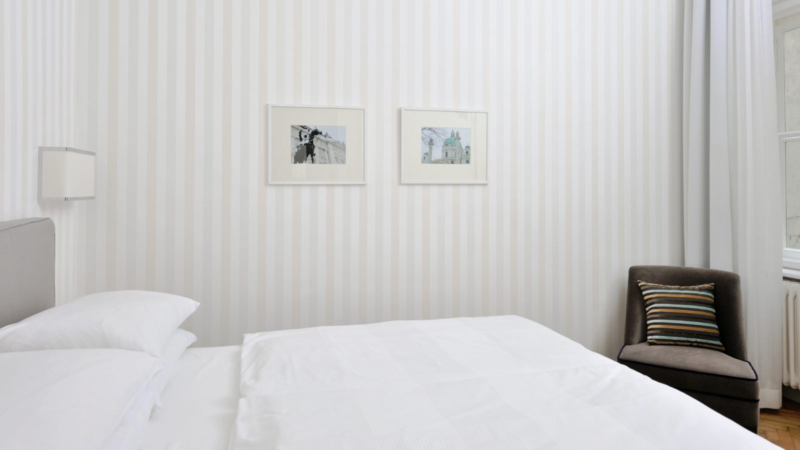 Helles Einzelzimmer im Hotel Kärntnerhof mit Streifentapete, zwei gerahmten Wien-Fotografien über dem Bett und Fauteuil am Fenster