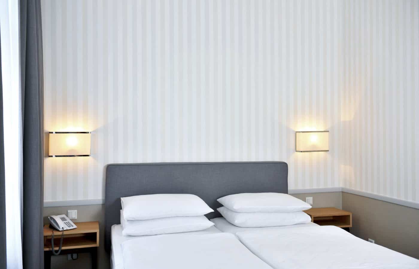 Doppelzimmer im Hotel Kärntnerhof mit gepolstertem Kopfteil, warmen Wandleuchten und heller Streifentapete