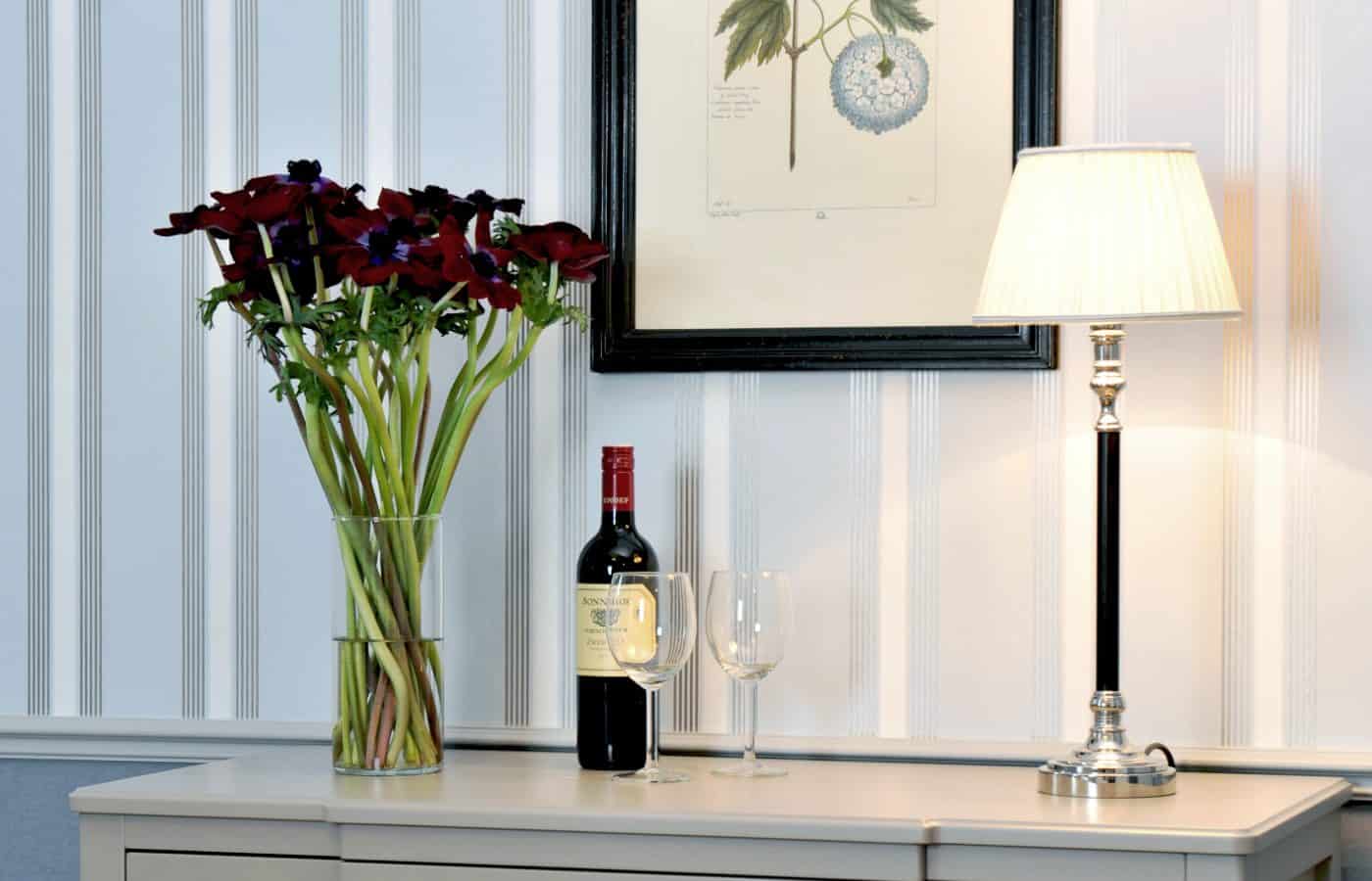 Kommode im Hotel Kärntnerhof mit dunkelroten Anemonen, Rotwein und Tischlampe