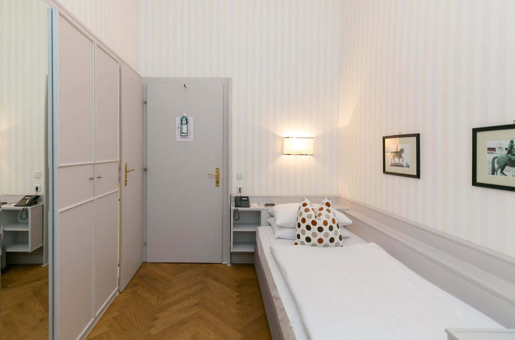 Einzelzimmer im Hotel Kärntnerhof mit schmalem Bett, Fischgrätparkett und zwei gerahmten Pferdebildern an der Wand