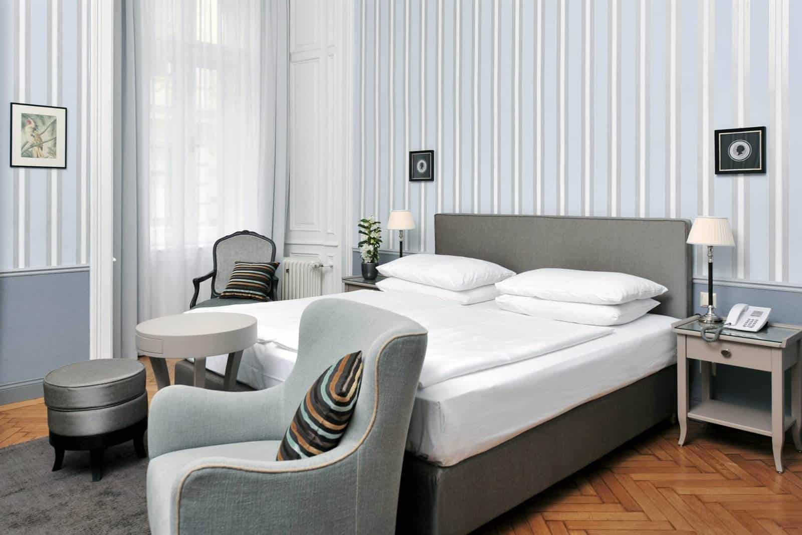 Doppelzimmer Large im Hotel Kärntnerhof mit Doppelbett, grauem Kopfteil, zwei hellblauen Fauteuils und rundem Beistelltisch auf Fischgrätparkett