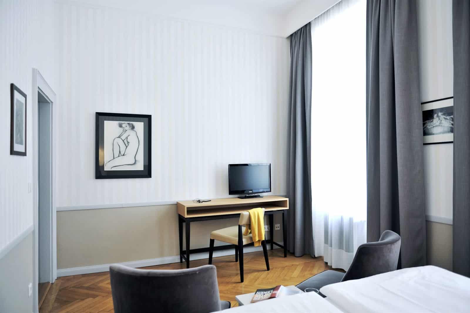 Doppelzimmer im Hotel Kärntnerhof mit Schreibtisch, Fernseher und gerahmter Aktzeichnung an der gestreiften Wand