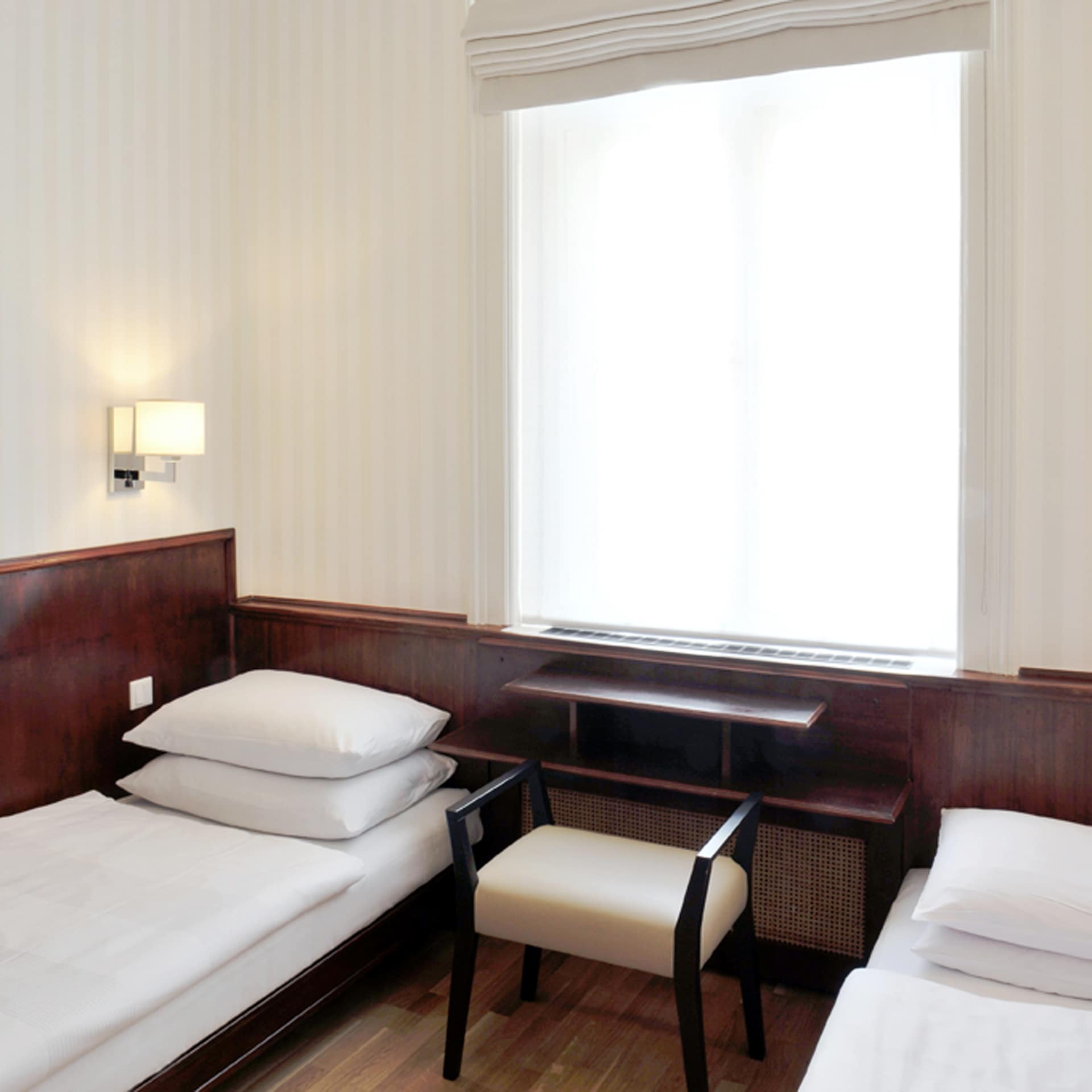 Zweibettzimmer Small im Hotel Kärntnerhof mit zwei getrennten Einzelbetten, dunkler Holzvertäfelung und hellem Fenster